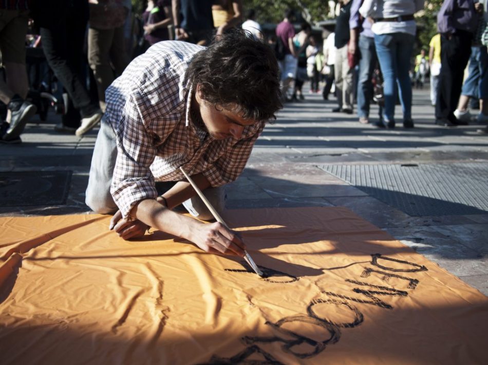 Un joven escribe una pancarta pidiendo "democracia real" en #acampadavalencia